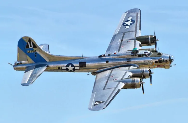 Stříbrný americký bombardér B-17 v letu pod modrou oblohou.