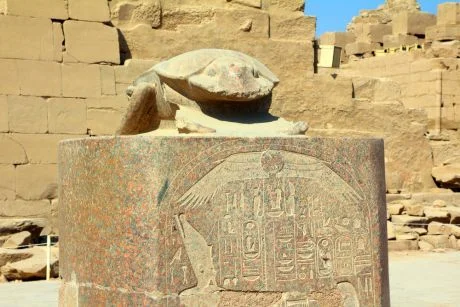 Kamenná socha egyptského skarabea na podstavci s hieroglyfy.