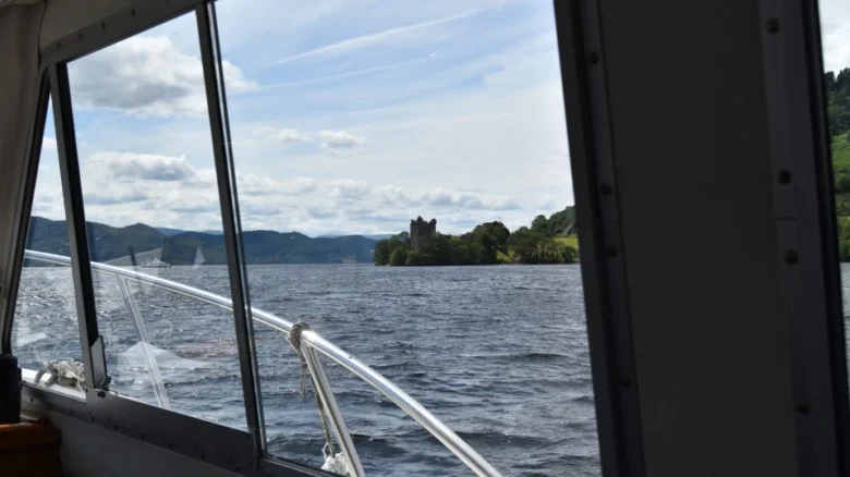 Vidina z lodi na loch ness s hradem v pozadí.