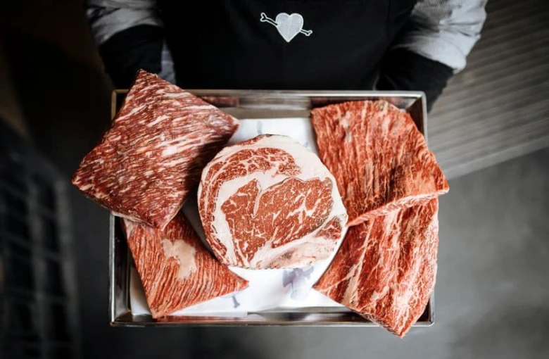 Tray s kusy mramorovaného vakuového masa Wagyu drží číšník.