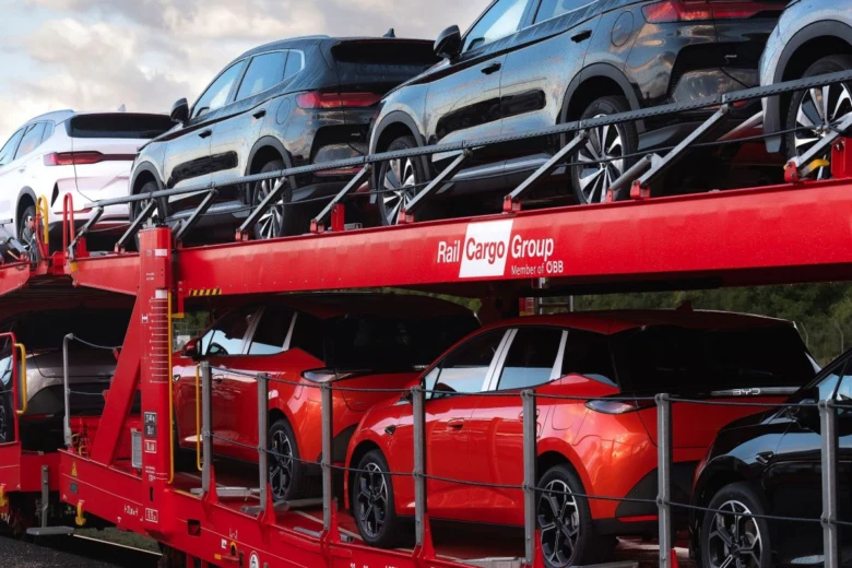 Červený nákladní vlak přepravující nové osobní automobily.